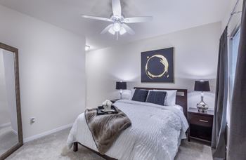 A bedroom with a large bed, a ceiling fan, and a painting on the wall.